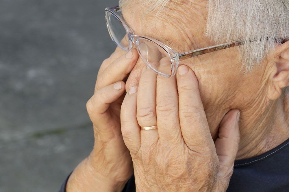 Eine ältere Frau mit Brille bedeckt ihr Gesicht mit den Händen.