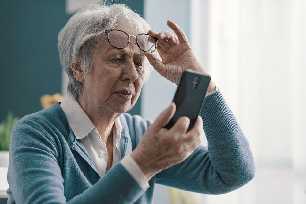Eine ältere Frau mit Brille schaut auf ihr Mobiltelefon.
