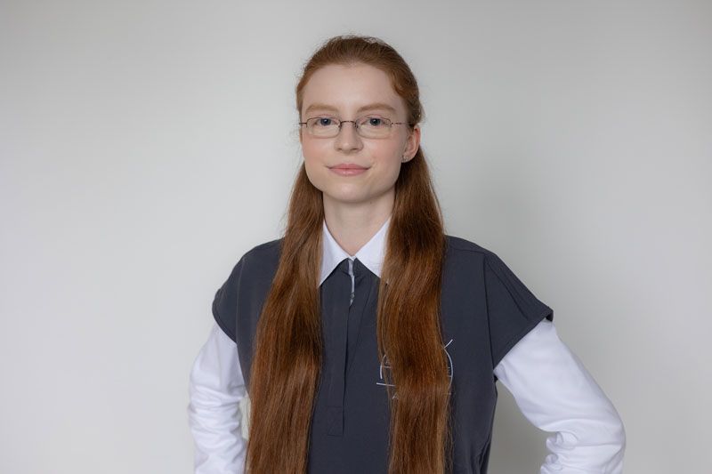 Eine Frau mit langen roten Haaren und Brille trägt ein weißes Hemd.