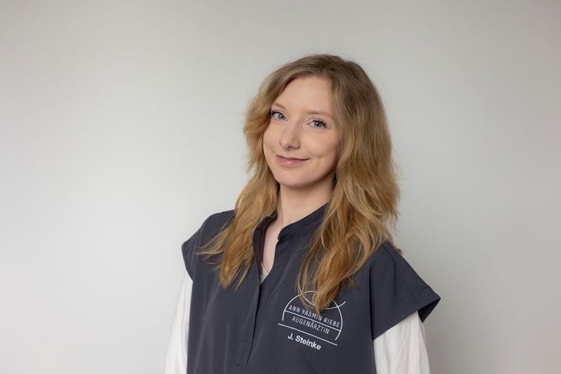Eine Frau mit grünen Haaren trägt einen weißen Pullover und lächelt.