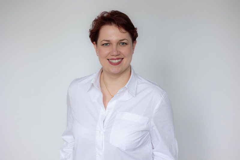 Eine Frau mit roten Haaren trägt ein weißes Hemd und lächelt.