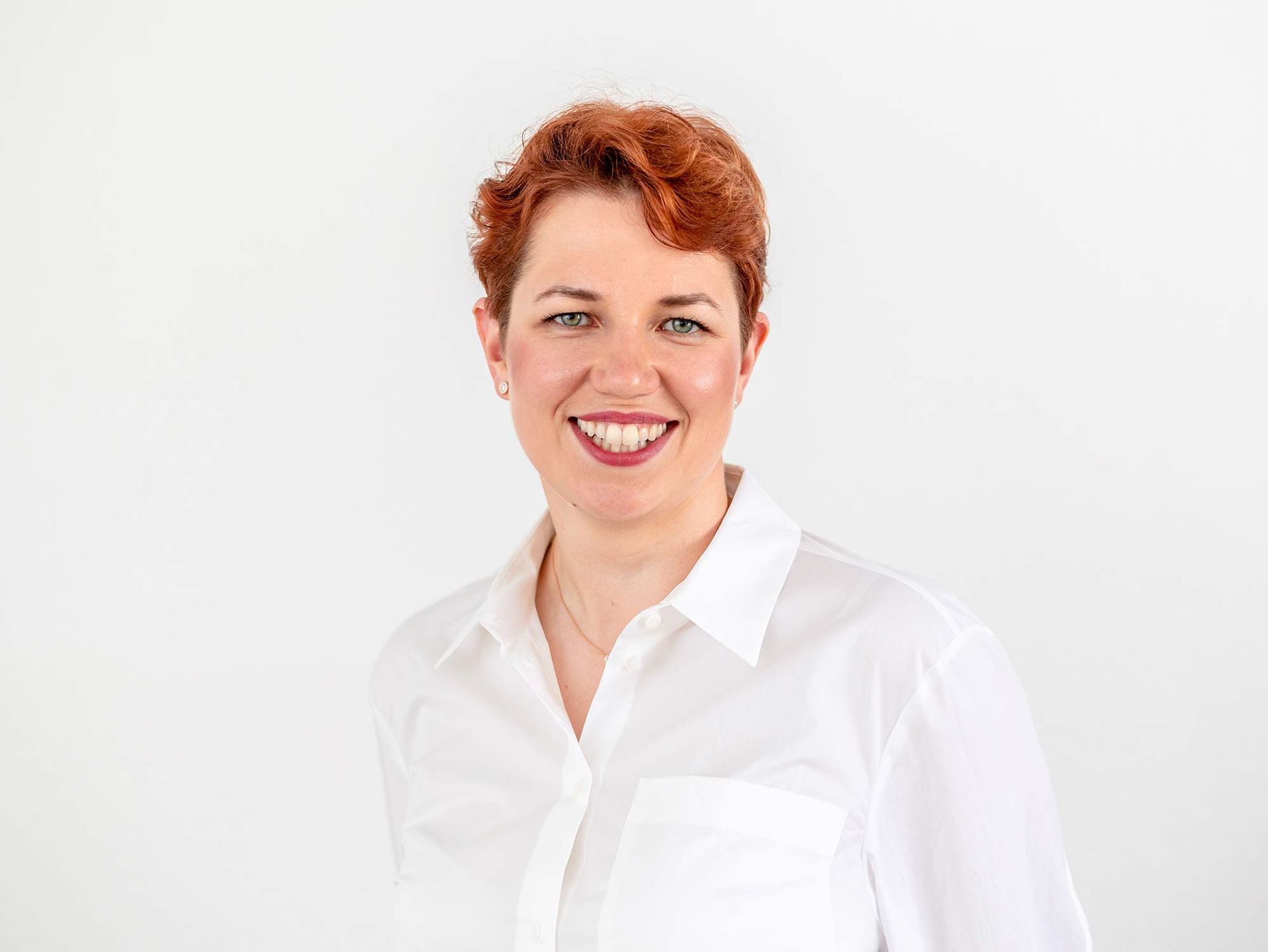 Eine Frau mit roten Haaren trägt ein weißes Hemd und lächelt.