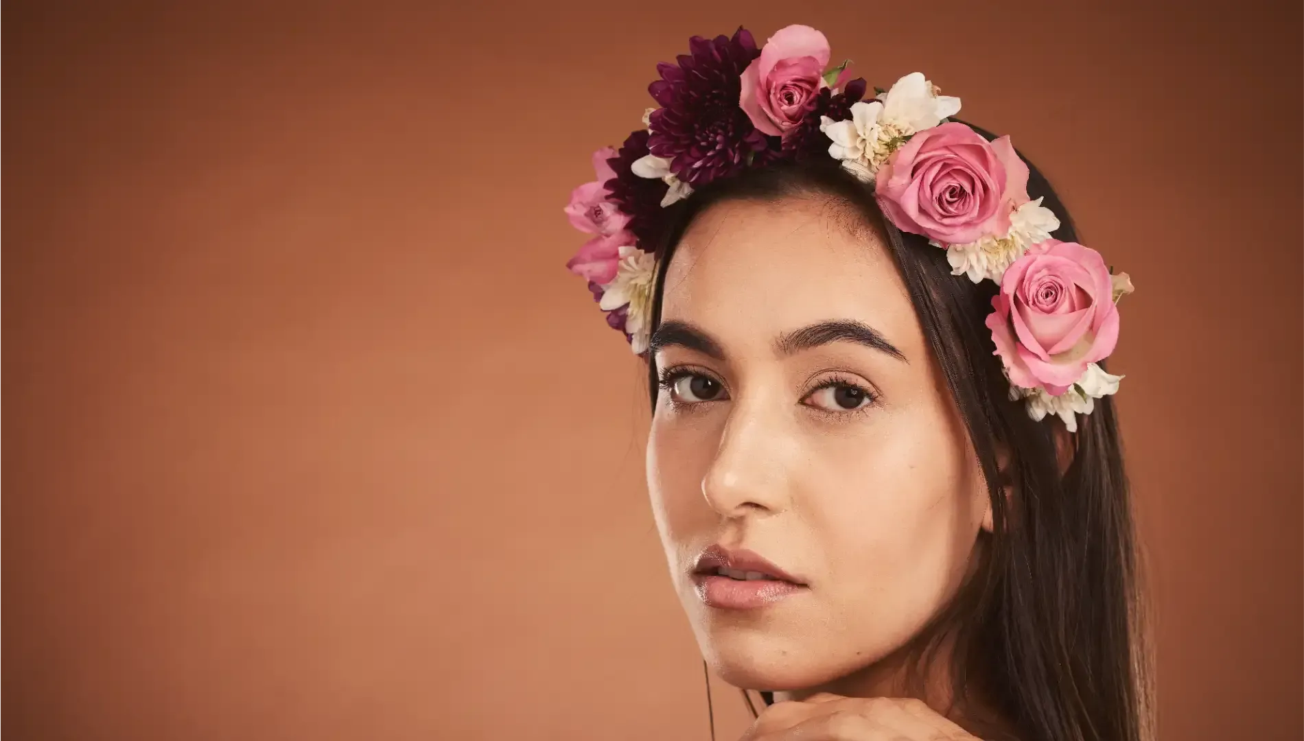 Mujer con corona floral, mirando hacia el espectador, sobre un fondo marrón.