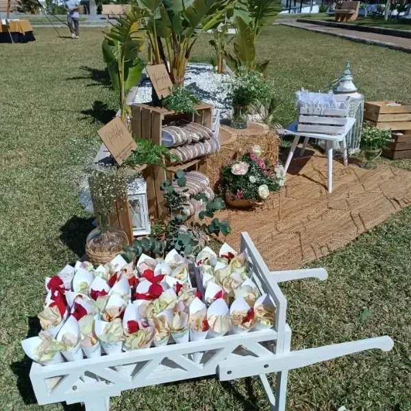 Decoración de boda con flores y conos de confeti en un carrito rústico en una zona verde.