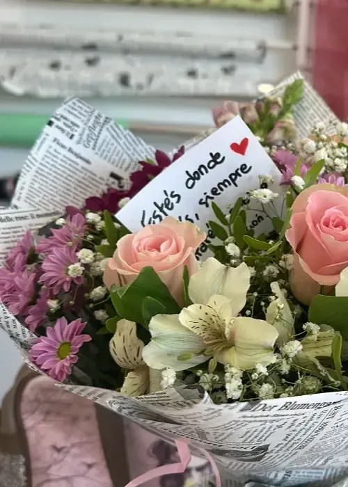 Ramo de rosas rosas y blancas, otras flores y nota que dice 