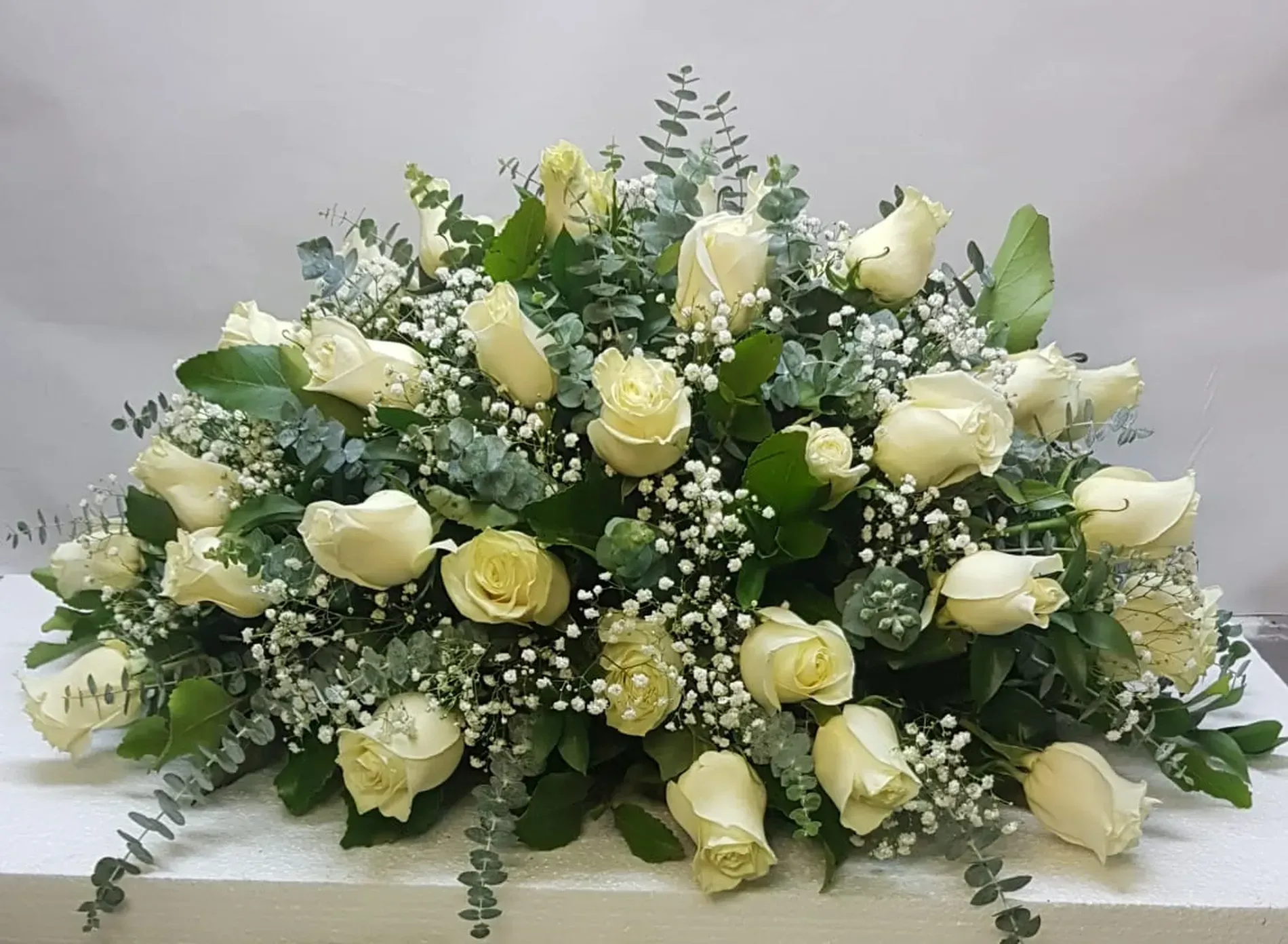 Rosas blancas y vegetación dispuestas en un arreglo floral bajo y rectangular.