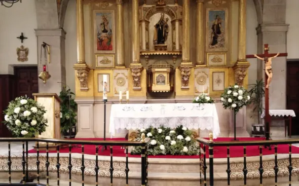 Altar de iglesia con decoraciones doradas, crucifijo y arreglos florales.