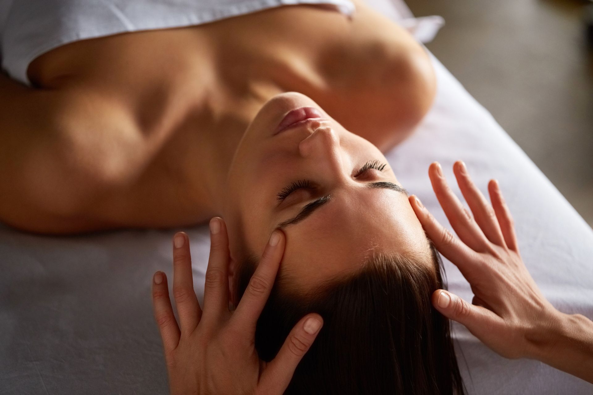 Mujer recibiendo un masaje facial con las manos en las sienes.