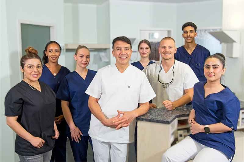 Zahnarztteam in OP-Kleidung, lächelnd, posiert in einer Klinik.