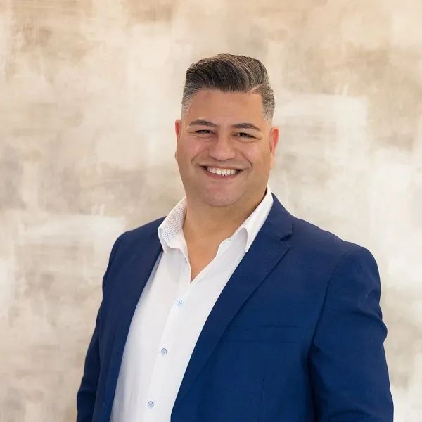Un hombre con traje azul y camisa blanca sonríe para la cámara.