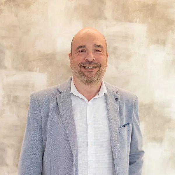 Un hombre con traje y camisa blanca sonríe para la cámara.