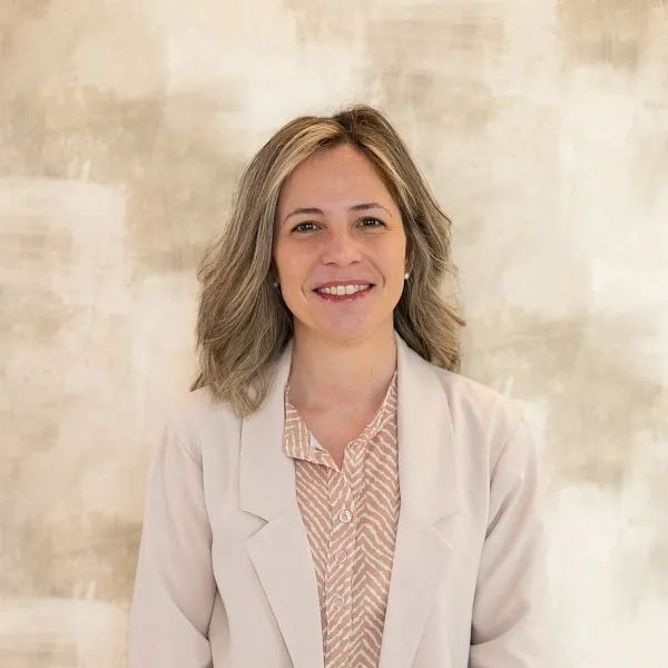 Una mujer con una chaqueta blanca y una camisa a rayas sonríe para la cámara.