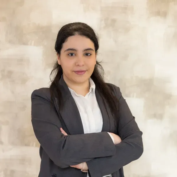 Una mujer con cabello largo y rizado está de pie con los brazos cruzados y sonriendo.