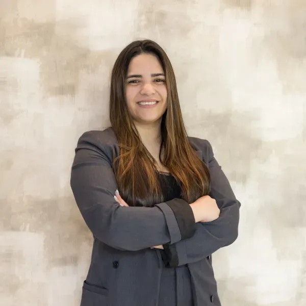 Una mujer con traje está parada con los brazos cruzados y sonriendo.