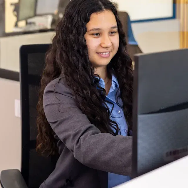 Una mujer está sentada frente a una computadora y sonriendo.