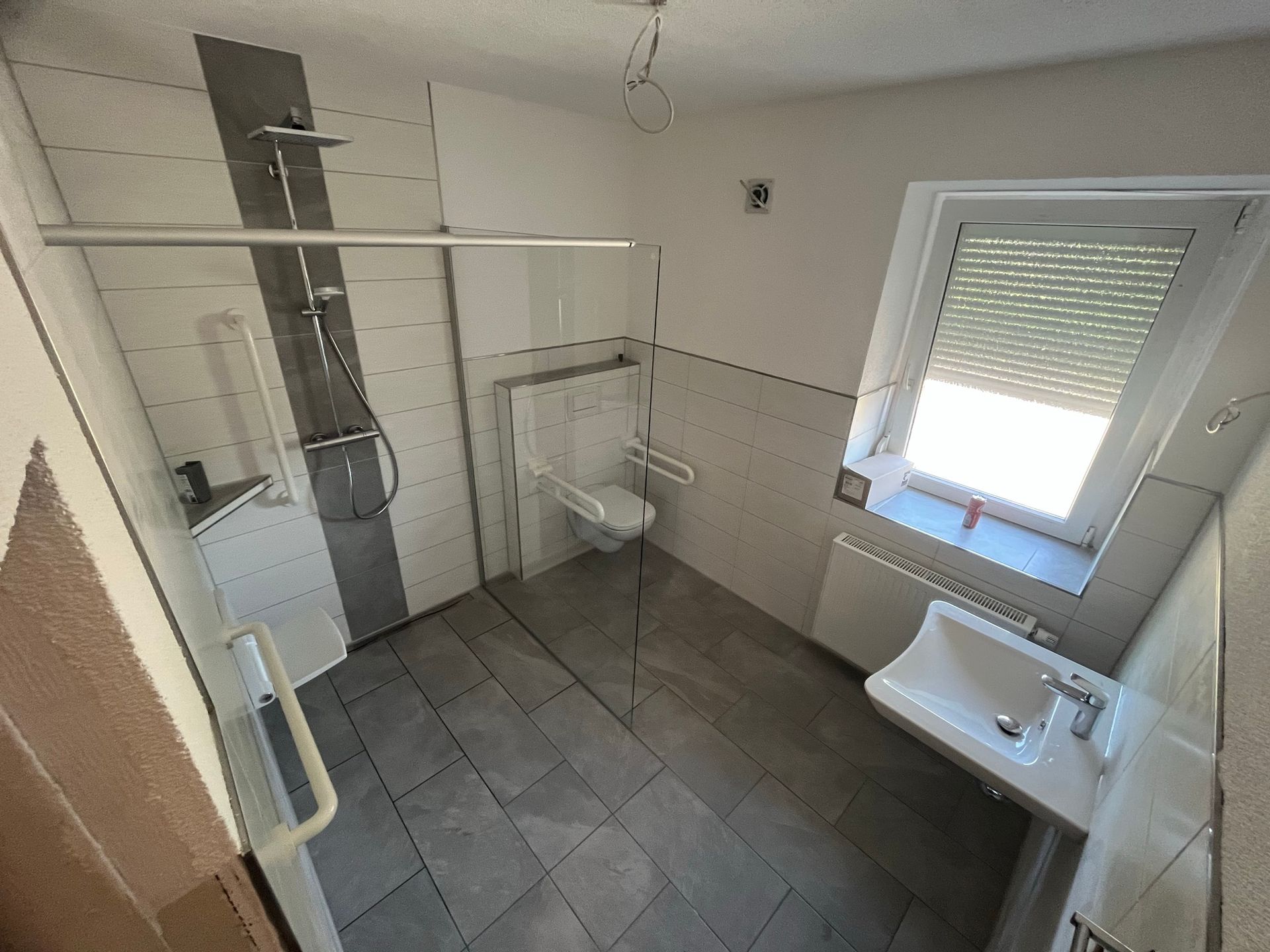 Ein Badezimmer mit ebenerdiger Dusche, Waschbecken, Toilette und Fenster.