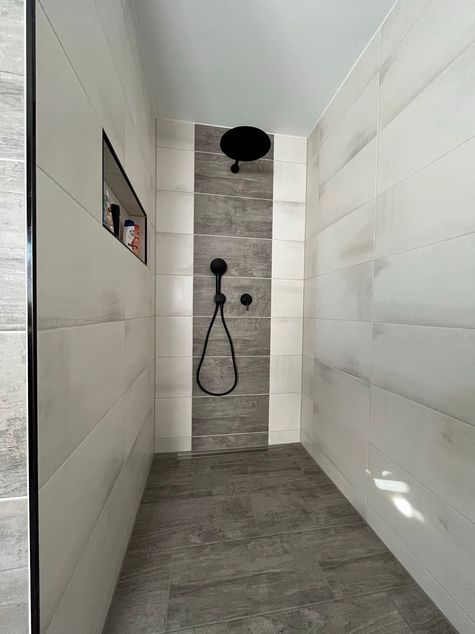 Ein Badezimmer mit ebenerdiger Dusche und schwarzem Duschkopf.