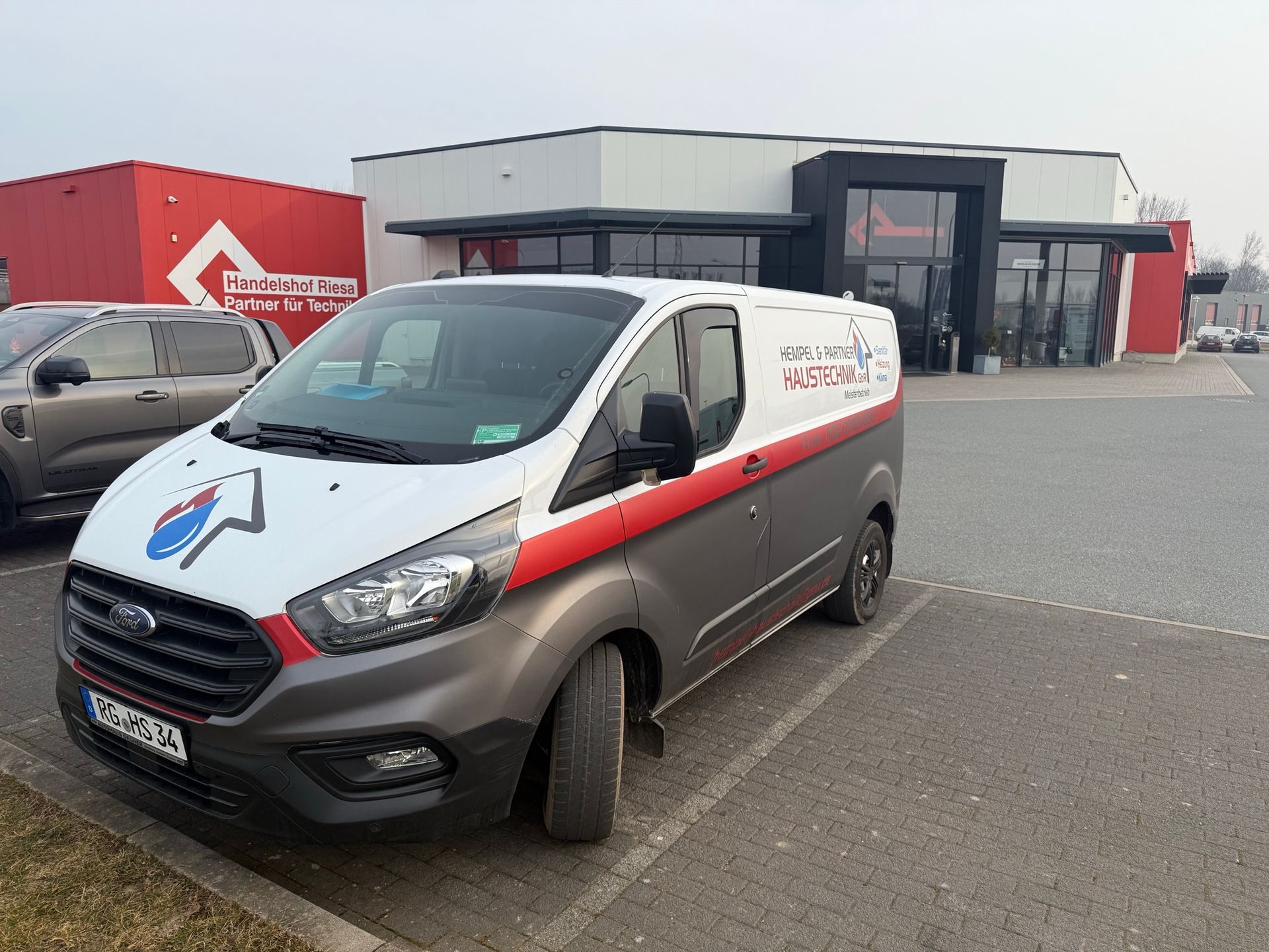 Ein weißer Lieferwagen steht auf einem Parkplatz vor einem Gebäude.