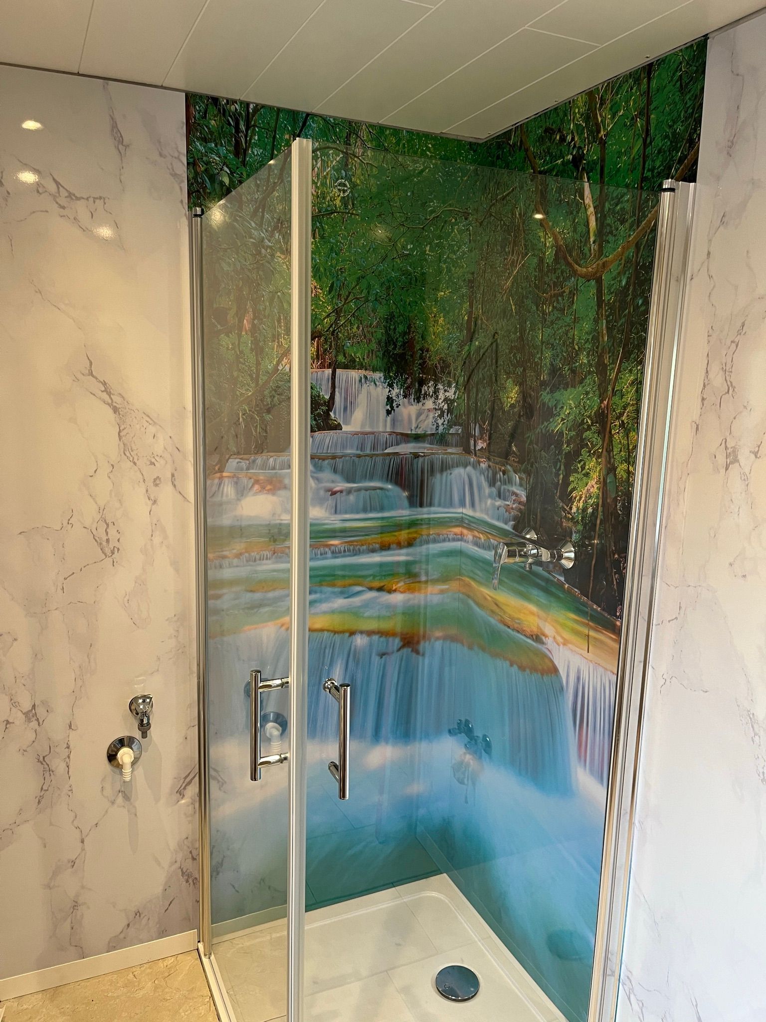 Ein Badezimmer mit einer Duschkabine und einem Bild eines Wasserfalls an der Wand.