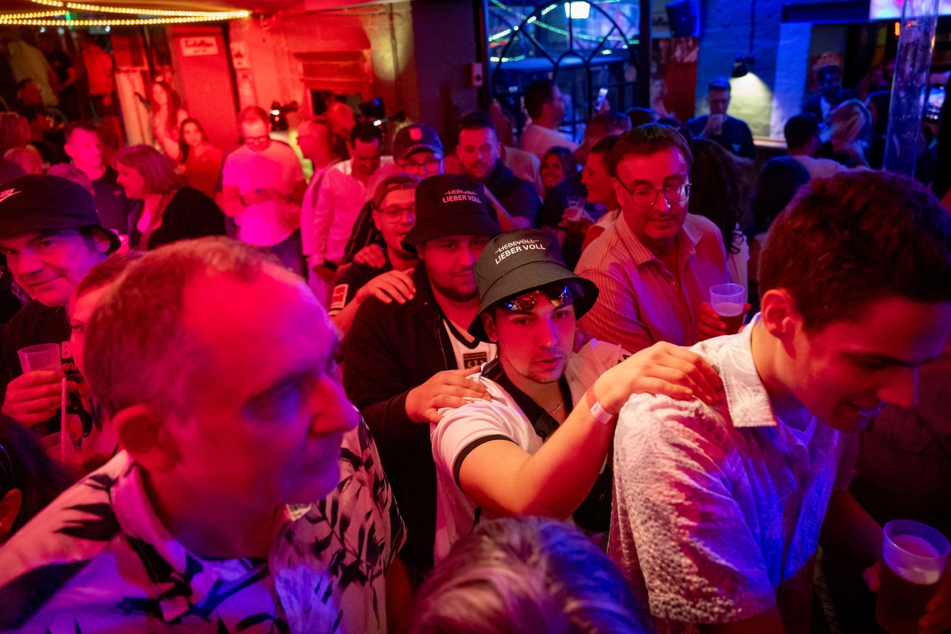 Ein überfüllter Nachtclub, in dem die Menschen unter rotem und violettem Licht dicht gedrängt stehen.