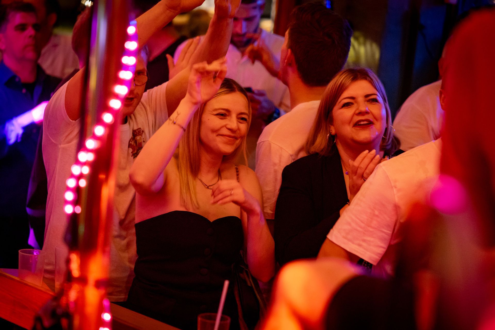 Menschen jubeln in einer neonbeleuchteten Menge, lächeln und heben die Hände bei einer Veranstaltung.