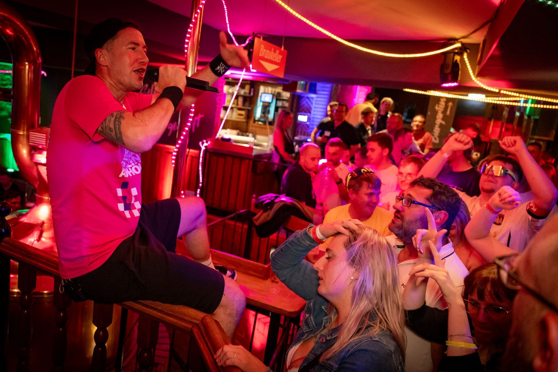 Sängerin tritt in einem rot beleuchteten Club auf, während die Menge jubelt und mit Handys filmt.