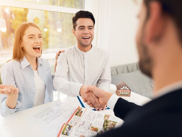 Un hombre y una mujer se dan la mano con un agente inmobiliario.