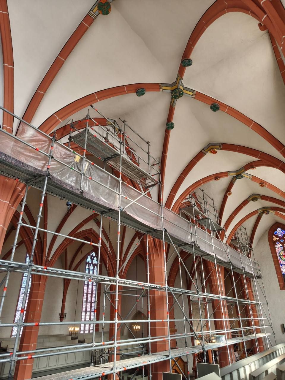 In einer Kirche im gotischen Stil mit hohen, rot gerippten Gewölbedecken steht eine metallene Gerüstkonstruktion.