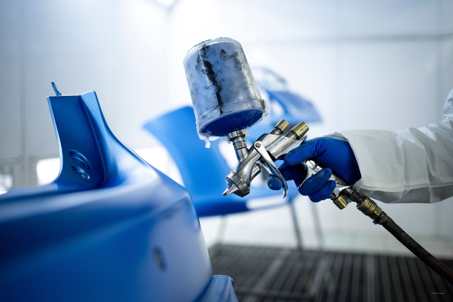 Fahrzeuglackierer lackiert Fahrzeugteile in einer Lackierkabine