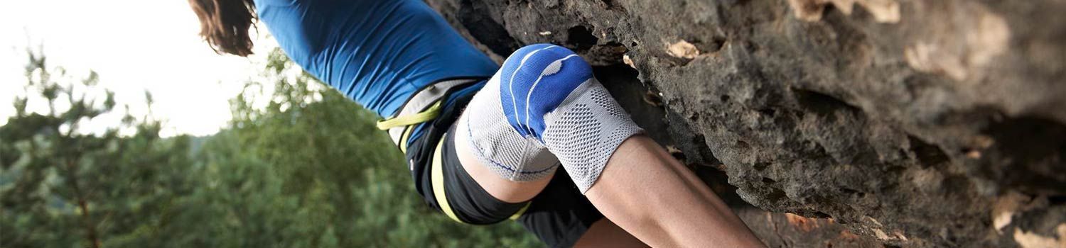 Eine Frau mit einem blauen Handschuh am Knie klettert auf einen Felsen.