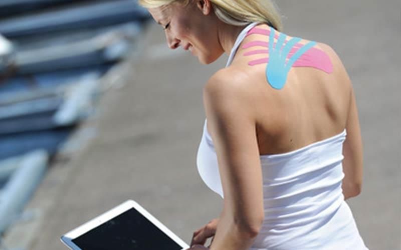 Eine Frau mit Kinesio-Tape auf dem Rücken benutzt ein Tablet.