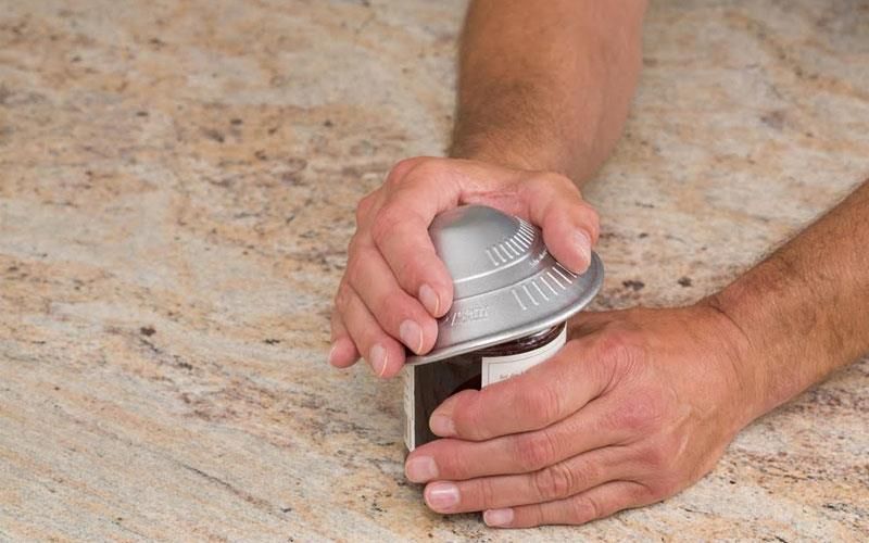 Eine Person öffnet mit einem Dosenöffner auf einer Theke eine Dose.