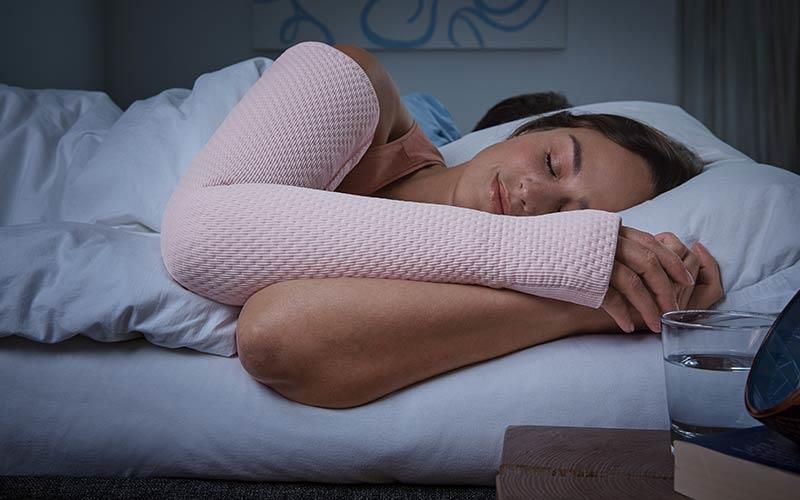 Eine Frau schläft in einem Bett und neben ihr steht ein Glas Wasser.