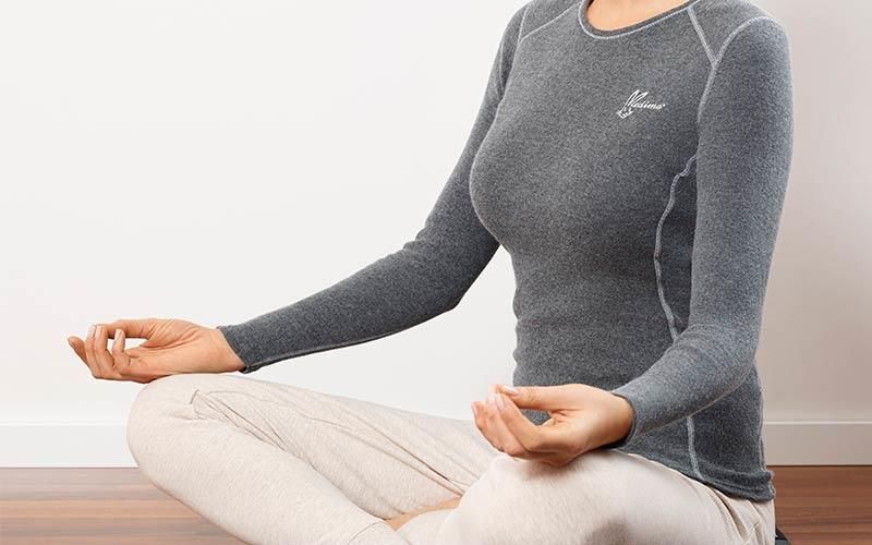 Eine Frau sitzt mit gekreuzten Beinen im Lotussitz auf dem Boden.