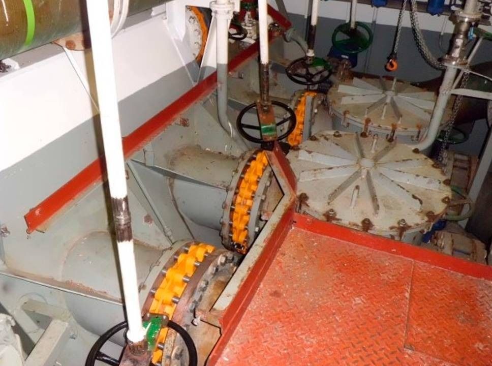 Teollisuuskoneen sisustus, jossa on oranssit ketjupyörät, harmaat metalliosat ja punainen lattia.