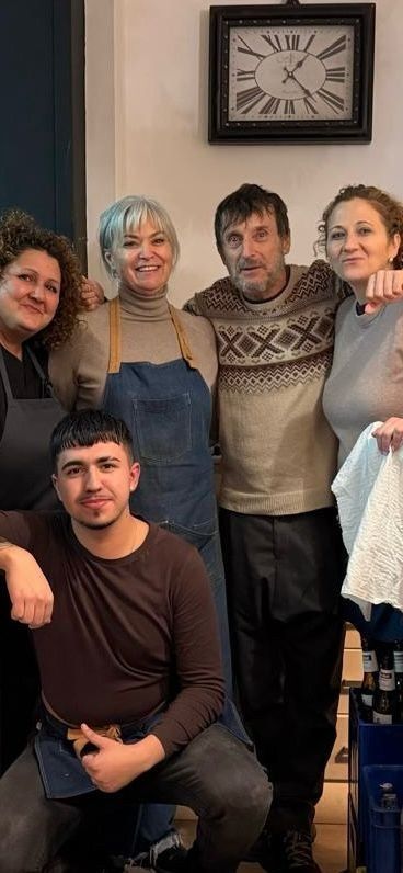 Cinco personas posando juntas en el interior de un edificio, debajo de un reloj de pared, sonriendo a la cámara.