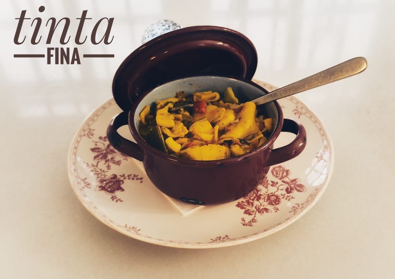 Cazuela pequeña de color morado sobre un plato floral con una cuchara, rellena con un plato horneado sobre un fondo claro.