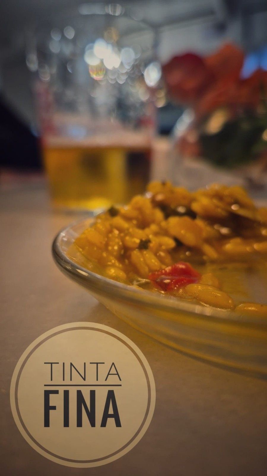 Plato de comida en primer plano y vaso de bebida al fondo, con el logo “Tinta Fina” en la esquina inferior.