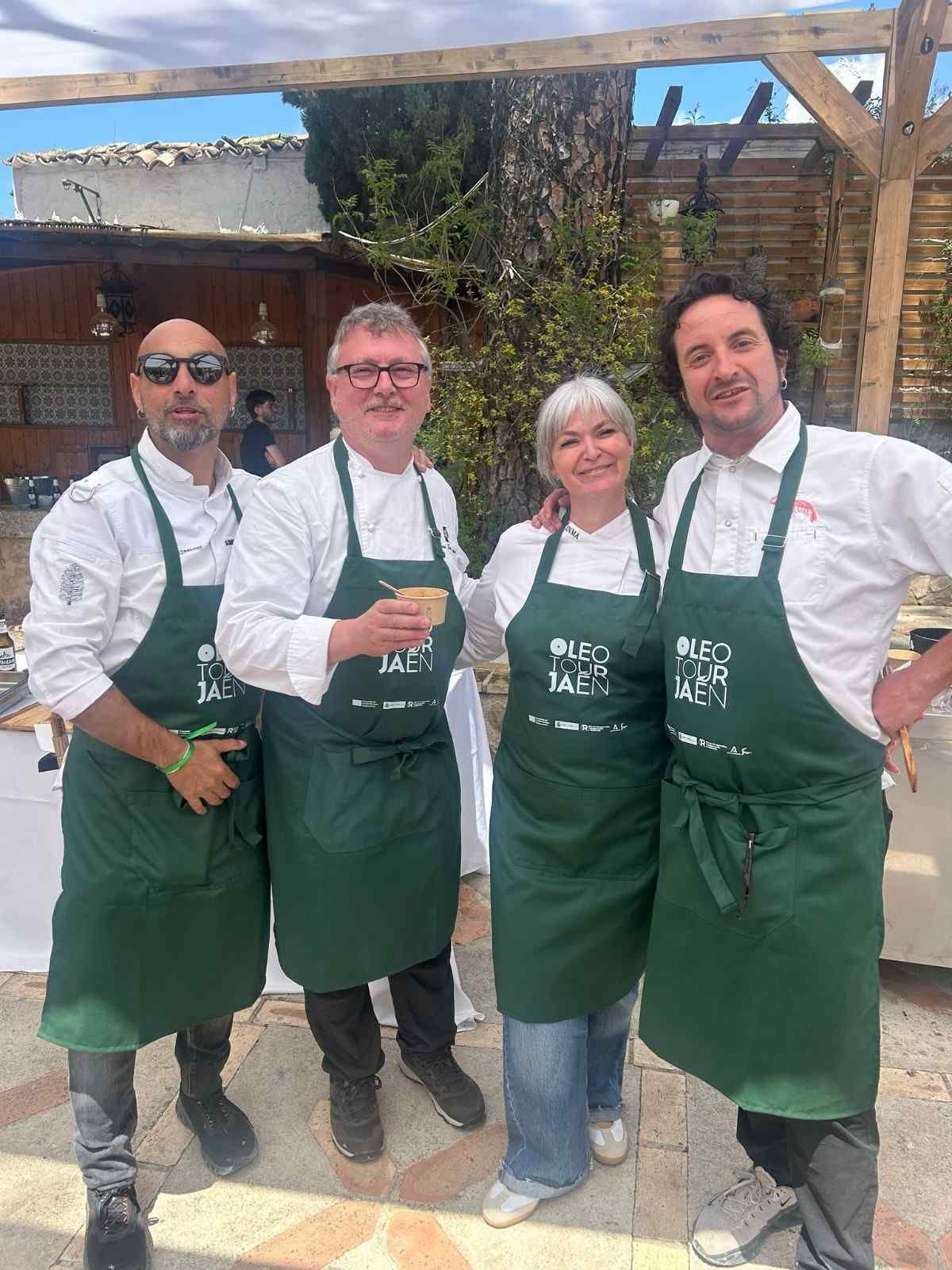 Cuatro personas con delantales verdes posan al aire libre, sosteniendo bebidas en un patio soleado.