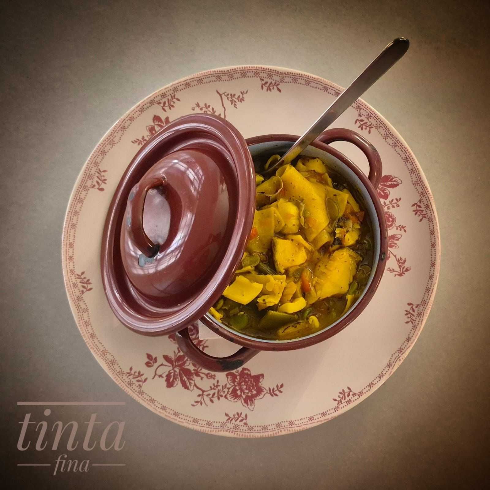 Bol decorativo de estofado amarillo con cuchara sobre un plato floral, visto desde arriba.