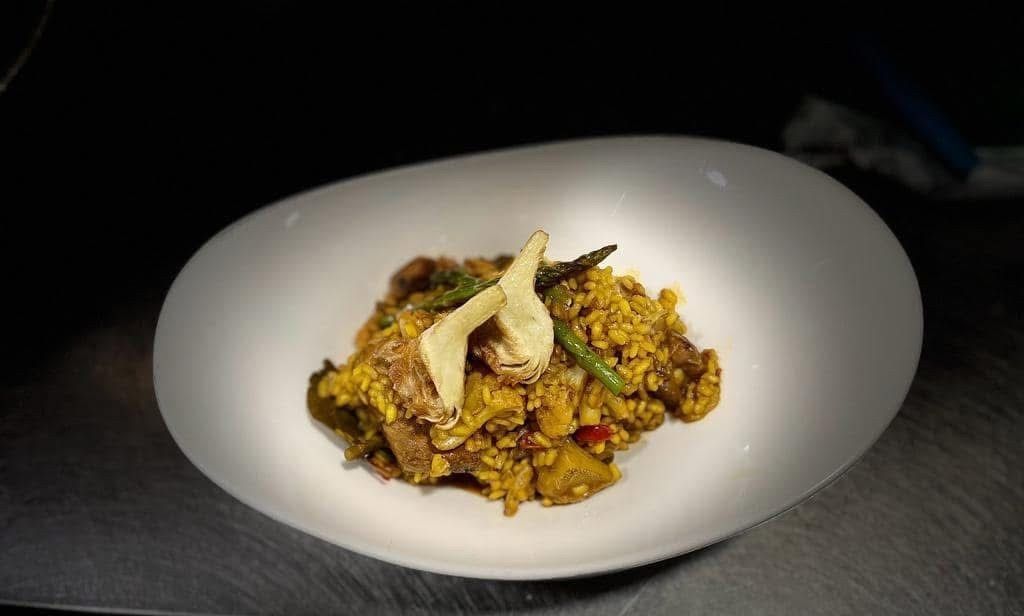 Plato de arroz mixto con especias y guarnición servido en un tazón blanco sobre una superficie oscura.