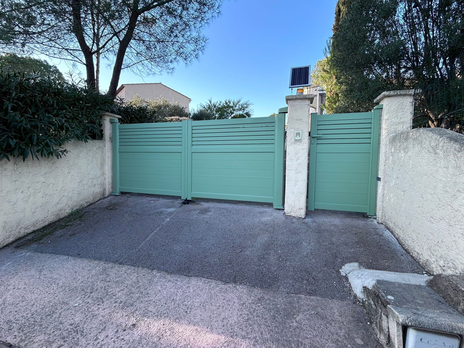 Un portail et un portillon en métal vert devant une allée.