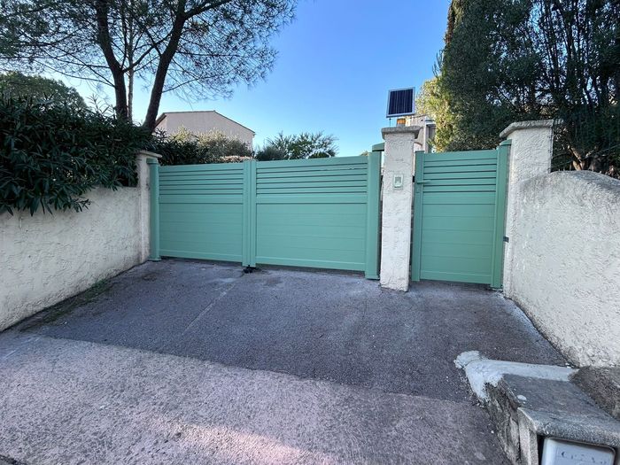 Un portail et un portillon en métal vert devant une allée.