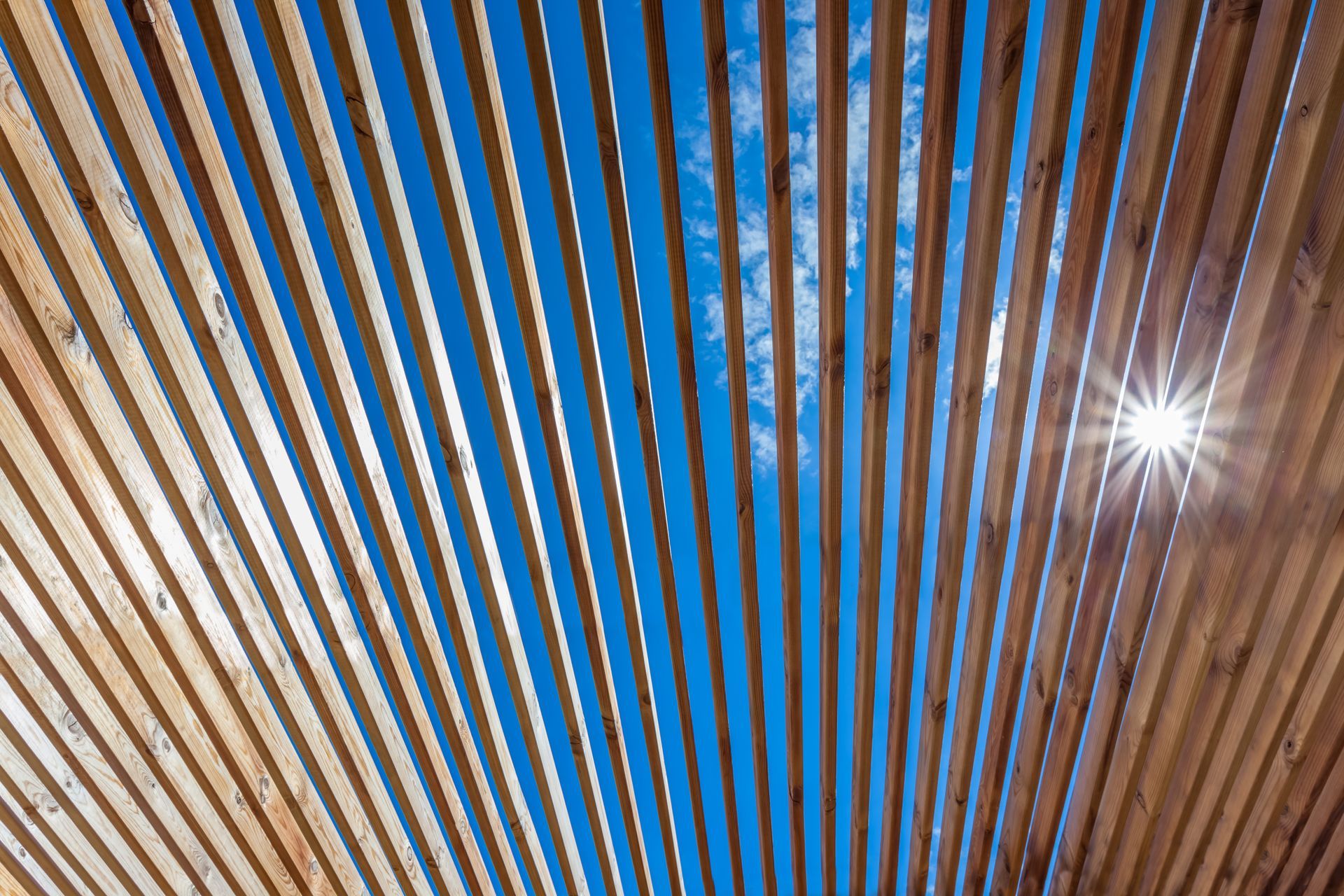 Vue du ciel bleu à travers les lames d'une pergola en bois.