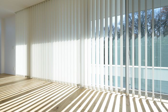 Pièce intérieure avec stores verticaux laissant passer la lumière du soleil qui projette des ombres rayées sur le parquet.