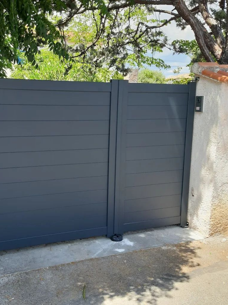 Portail à lattes horizontales grises, fermé, devant un mur clair.