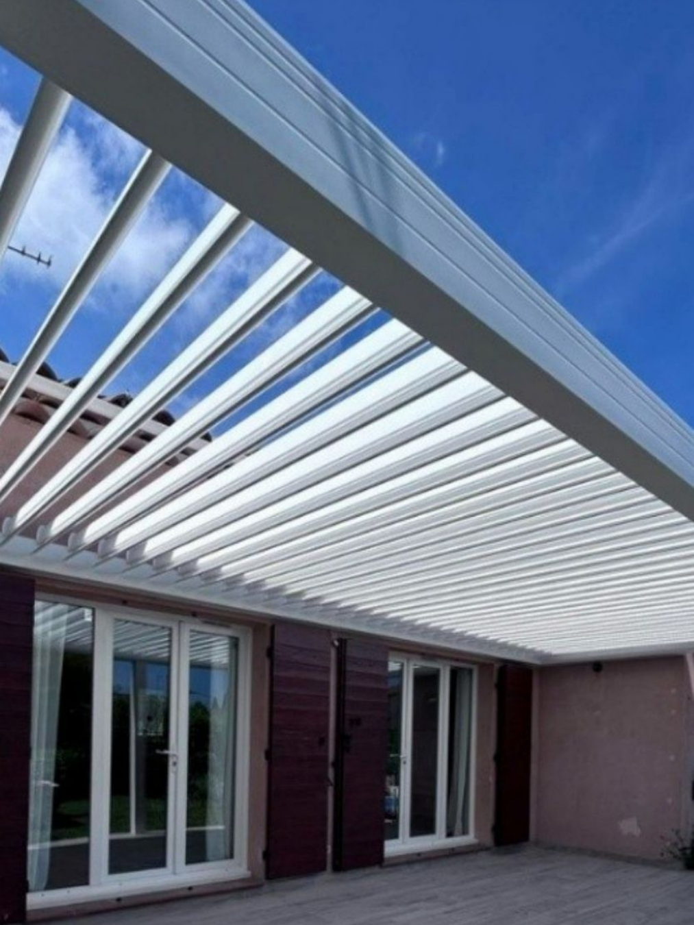 Pergola bioclimatique en aluminium blanc au-dessus d'un patio avec fenêtres.