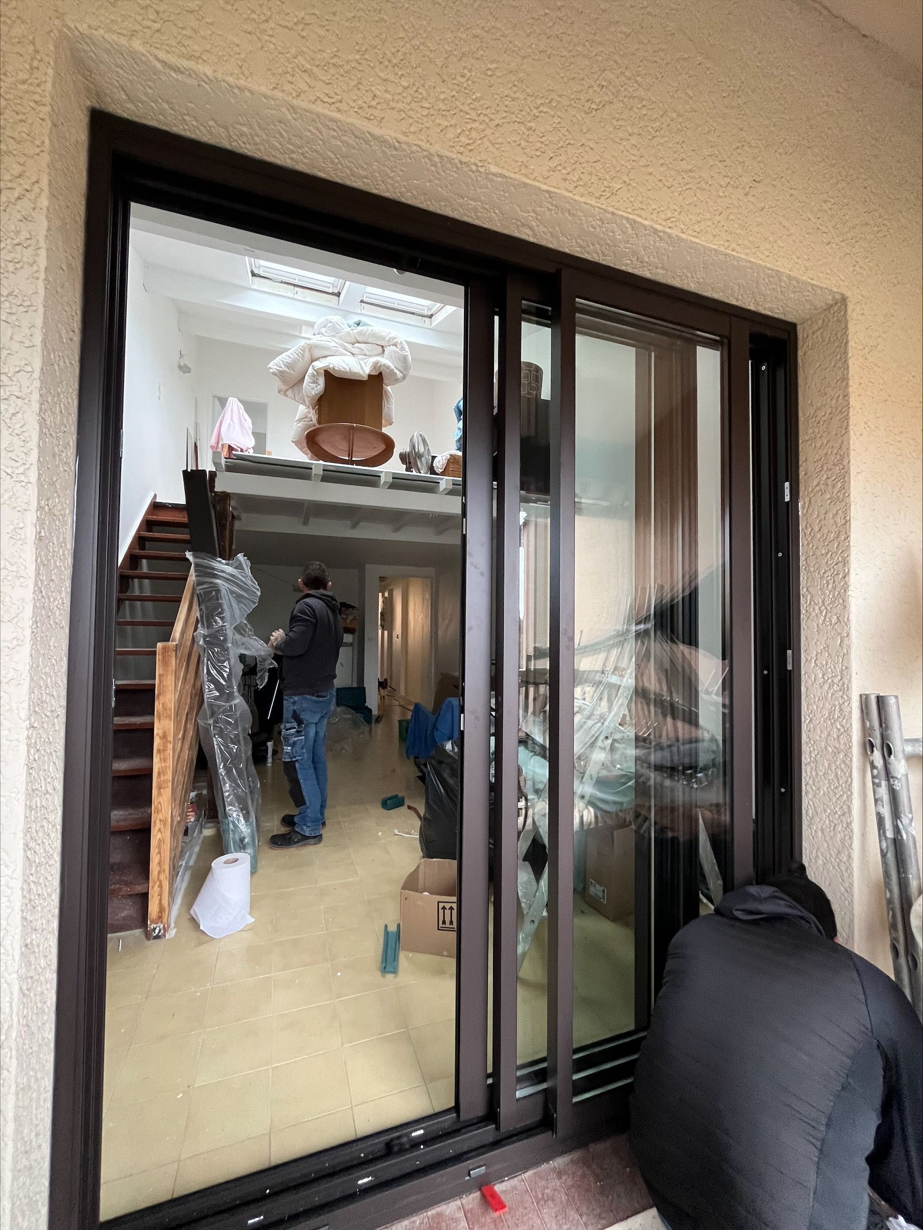 Baie vitrée à cadres bruns. Une personne est agenouillée, en train de travailler. Intérieur avec des personnes et des objets visibles.