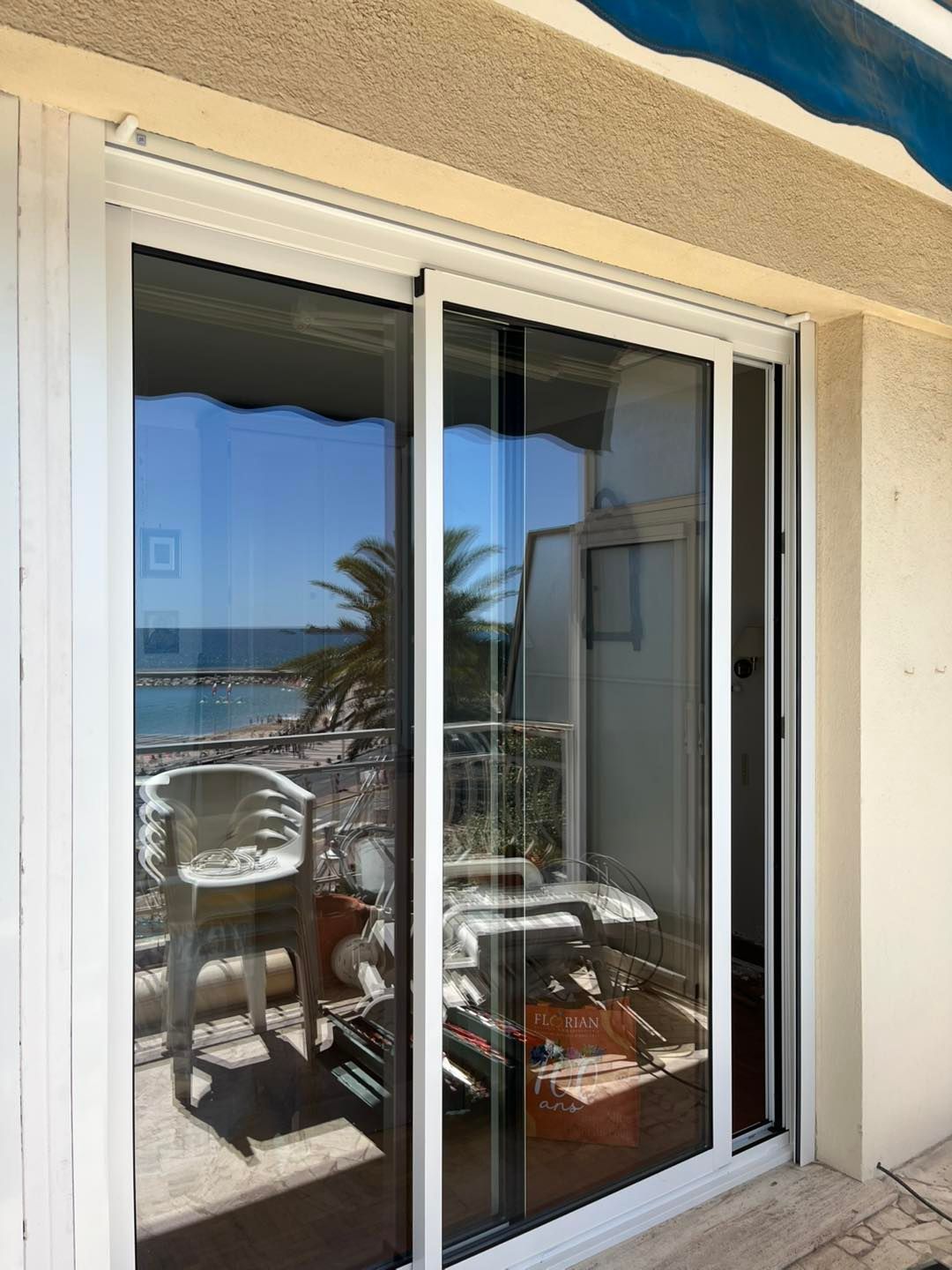 Baie vitrée en aluminium de couleur blanche, donnant sur un balcon avec vue sur la plage.