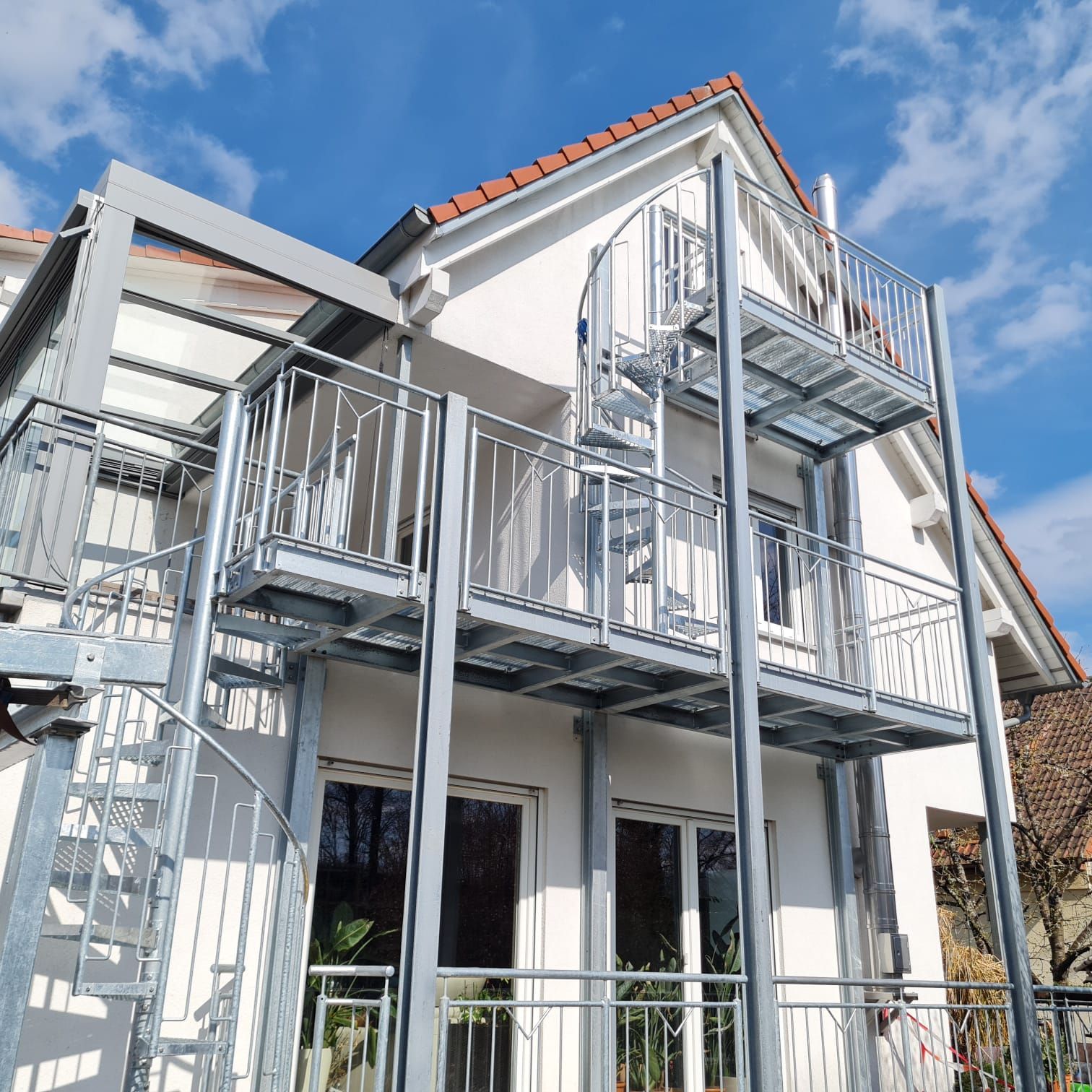Eine Holztreppe mit Glasgeländer und integrierter Beleuchtung führt an einer weißen Wand empor.